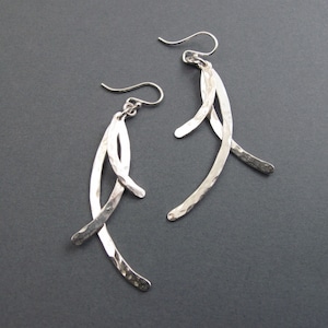 May include: A pair of silver dangle earrings with a hammered finish. The earrings are made of multiple curved pieces of metal that are connected together.