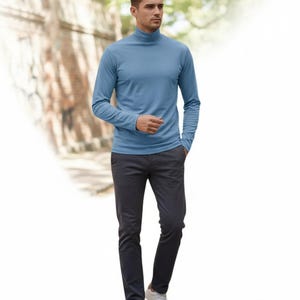 May include: A light blue turtleneck long-sleeve shirt paired with dark gray pants and white sneakers. The outfit is simple and casual, suitable for everyday wear. The model is walking in front of a blurred background of a building and trees.