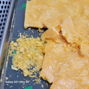 May include: Close-up of a tray with pieces of yellow-orange wax. Some pieces are broken into smaller fragments, while others are larger, rectangular shapes. The wax has a textured, crystalline appearance.