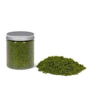 May include: A clear plastic jar with a silver lid filled with green granular material, next to a pile of the same material. The material appears to be a fine, textured substance, possibly for crafts or model making.