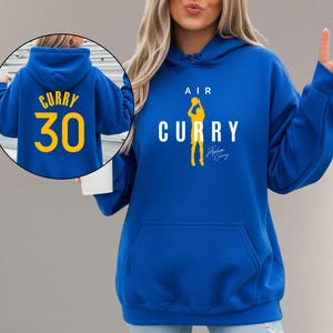 May include: Royal blue hoodie with a front pocket and a hood. The front features the text "AIR CURRY" with a yellow silhouette of a basketball player. The back of the hoodie has the name "CURRY" and the number "30" in yellow.