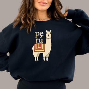 May include: Black sweatshirt with a white llama wearing a red and yellow saddle. The text "pe ru" is printed in gold above the llama.