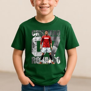 May include: A dark green short-sleeved t-shirt featuring a graphic print of Cristiano Ronaldo in a red jersey and white shorts. The design includes the text CRISTIANO RONALDO and the number 07 in a large font, with a soccer ball at the bottom.