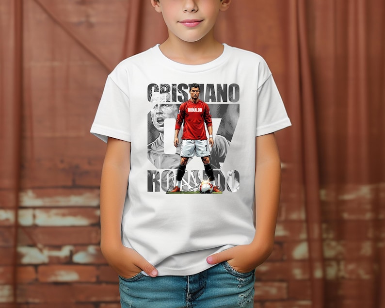 May include: A white short-sleeved t-shirt featuring a graphic print of Cristiano Ronaldo in a red jersey and white shorts. The design includes the text CRISTIANO RONALDO in bold black letters, a black and white portrait, and a soccer ball at the feet.