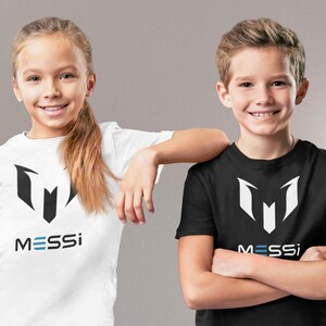 May include: Two children wearing white and black t-shirts with a black and white logo and the word "MESSI" printed on the front.