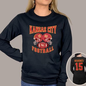 May include: Black long-sleeve shirt with the text "Kansas City Football" and a graphic of two football helmets with the numbers 19 and 60. The shirt also features a football with the letters "KC".