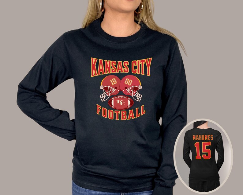 May include: Black long-sleeve shirt with the text "Kansas City Football" and a graphic of two football helmets with the numbers 19 and 60. The shirt also features a football with the letters "KC".
