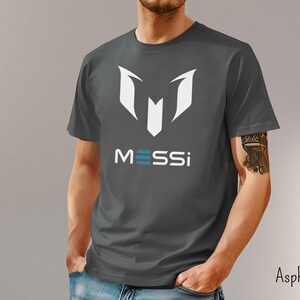 May include: A dark gray t-shirt with a white graphic of the letter "M" and the word "MESSI" in white and blue letters.