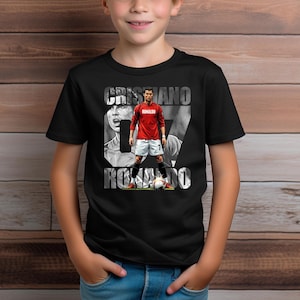 May include: A black short-sleeve t-shirt featuring a graphic print of Cristiano Ronaldo in a red jersey and white shorts, standing with a soccer ball. The text CRISTIANO RONALDO is printed in large white letters behind the player figure.