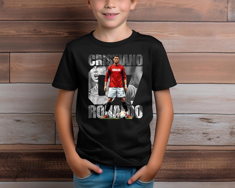 May include: A black short-sleeve t-shirt featuring a graphic print of Cristiano Ronaldo in a red jersey and white shorts, standing with a soccer ball. The text CRISTIANO RONALDO is printed in large white letters behind the player figure.