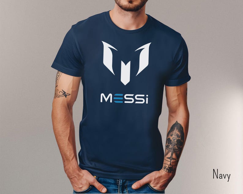 May include: Navy blue t-shirt with a white graphic of a stylized "M" and the word "MESSI" in blue and white letters.