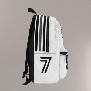 May include: White backpack with black and gray vertical stripes on the side. The number "7" is printed in black on the front. The backpack has a black handle and straps.
