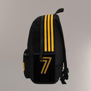 May include: Black backpack with yellow stripes and the number 7. The backpack has a side pocket with the number 7 in yellow. The backpack has a top handle and a front pocket.