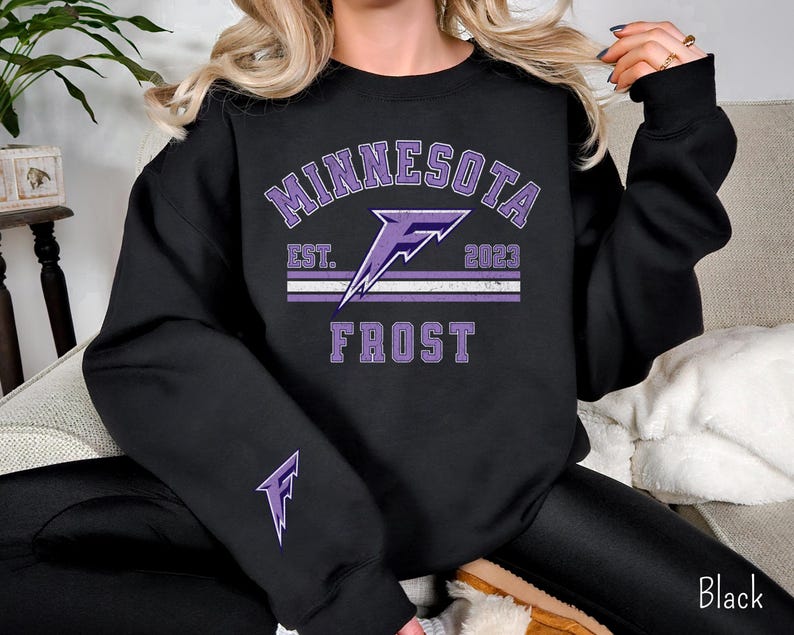 Pode incluir: Camisola de moletom preta com um design gr&aacute;fico roxo que diz "Minnesota Frost" com um raio e o texto "Est. 2023".
