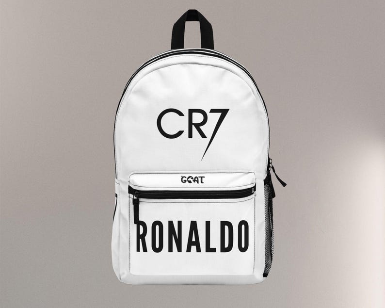May include: White backpack with black accents, featuring the text "CR7" and "RONALDO" in bold black letters. The word "GOAT" is also printed on the front pocket. Includes a black handle and a side mesh pocket.
