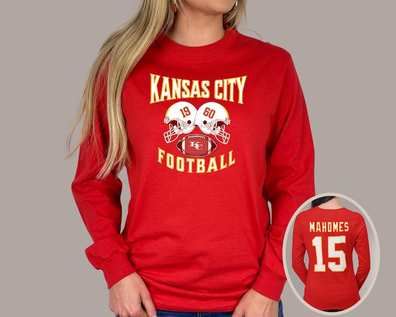 May include: Red long-sleeve t-shirt with the text "Kansas City Football" and a graphic of two football helmets with a football in the middle. The helmets have the numbers 19 and 60 on them.