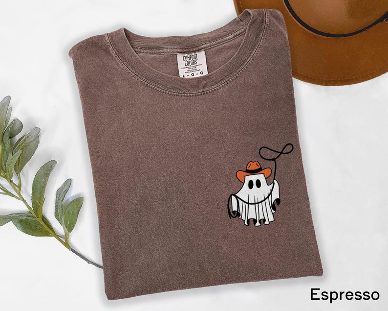 K&ouml;nnte beinhalten: Espressofarbenes T-Shirt mit einer Grafik eines Geistes, der einen Cowboyhut tr&auml;gt und ein Lasso h&auml;lt. Das Shirt besteht aus weichem Material und hat einen Rundhalsausschnitt. Das Comfort Colors-Etikett ist innen am Kragen sichtbar.