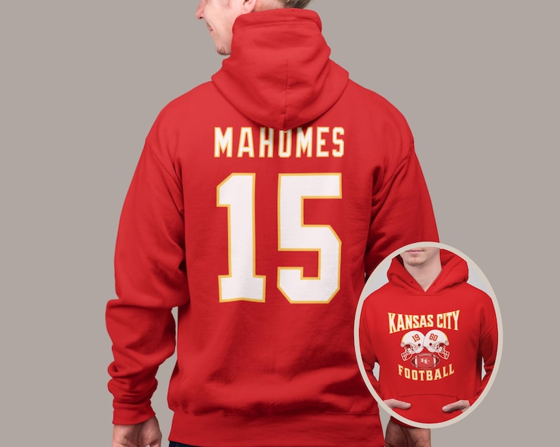 May include: Red hooded sweatshirt with the name "Mahomes" and the number "15" printed on the back in white. The front of the sweatshirt has a smaller image of two football helmets with the text "Kansas City Football" printed below.