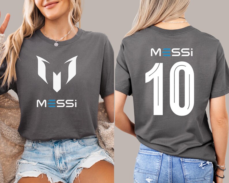 May include: A gray t-shirt with a white graphic of the letter "M" and the word "MESSI" on the front. The back of the shirt has the number "10" and the word "MESSI" in white.