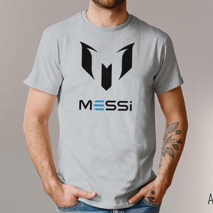 May include: A gray t-shirt with a black graphic of a soccer jersey and the word "MESSI" in blue letters.