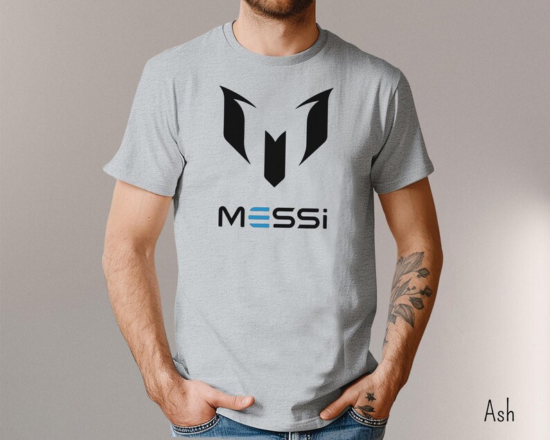 May include: A gray t-shirt with a black graphic of a soccer jersey and the word "MESSI" in blue letters.