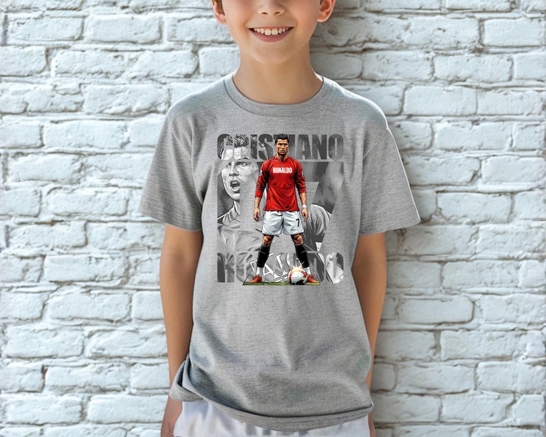 May include: A heather gray short-sleeve t-shirt featuring a graphic print of Cristiano Ronaldo in a red jersey and white shorts. The design includes a large black and white portrait background and the text CRISTIANO RONALDO in bold letters.