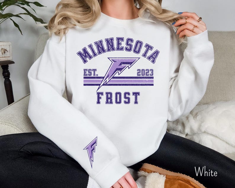 Pode incluir: Camisola branca com um design gr&aacute;fico roxo e branco que diz "Minnesota Frost" com um logotipo de raio e o texto "Est. 2023".