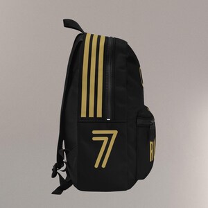 May include: Black backpack with gold accents, including three vertical stripes and the number 7. Features a zippered main compartment, a front pocket, and adjustable straps. The backpack has a top handle for carrying.