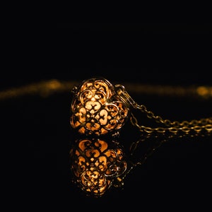 May include: A gold necklace with a delicate, intricate heart-shaped pendant. The pendant is openwork and has a light inside, creating a warm glow.