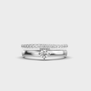 Puede incluir: Dos anillos de plata. El anillo superior es una banda de pequeñas piedras transparentes. El anillo inferior tiene una sola piedra transparente más grande en el centro. Los anillos están sobre un fondo blanco.