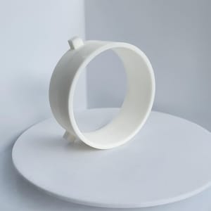 May include: White plastic ring with a smooth, rounded surface and two small, square protrusions on either side.