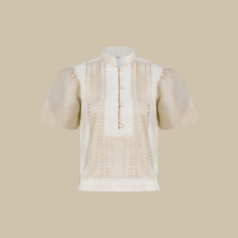 K&ouml;nnte beinhalten: Ein wei&szlig;es Leinenhemd mit Stehkragen und kurzen &Auml;rmeln. Das Hemd hat ein zartes Stickmuster in beige.