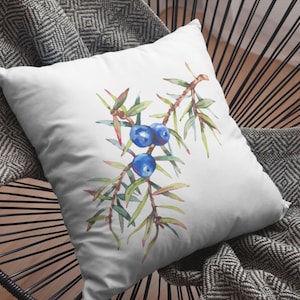 May include: A white throw pillow with a watercolor illustration of juniper berries and branches. The berries are blue and the branches are green.