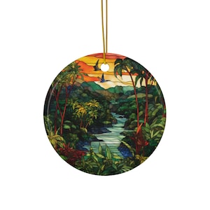 Può includere: Un ornamento rotondo in ceramica con un'immagine in stile vetrata di una scena di giungla tropicale con un fiume che scorre attraverso di essa. La scena è ambientata al tramonto con un cielo vibrante arancione, giallo e rosso. Ci sono palme, una lussureggiante vegetazione verde e uccelli che volano sopra.