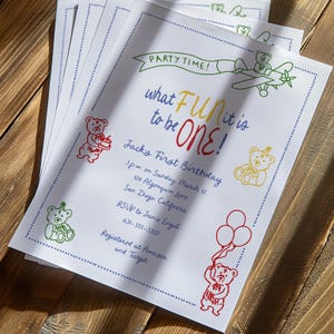 Puede incluir: Invitaciones blancas con borde punteado azul e ilustraciones de ositos de peluche coloridos. El texto dice "Party Time!" y "What FUN it is to be ONE!" con detalles del evento. Las invitaciones son para un primer cumplea&ntilde;os.