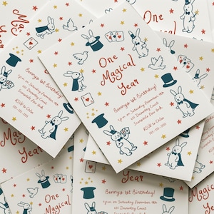 Puede incluir: Un conjunto de invitaciones cuadradas con temática mágica. Cada invitación presenta ilustraciones de conejos, naipes, palomas y sombreros de copa. El texto dice "One Magical Year" e incluye detalles del evento.