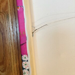 May include: The back of a canvas painting with a wooden frame. A wire is attached to the frame with a hook for hanging.