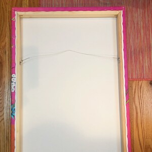 May include: The back of a framed canvas painting with a pink and white patterned border. The canvas is stretched over a wooden frame and has a wire attached for hanging.