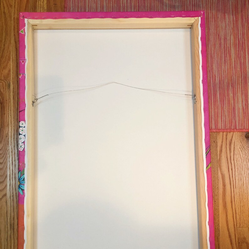 May include: The back of a framed canvas painting with a pink and white patterned border. The canvas is stretched over a wooden frame and has a wire attached for hanging.