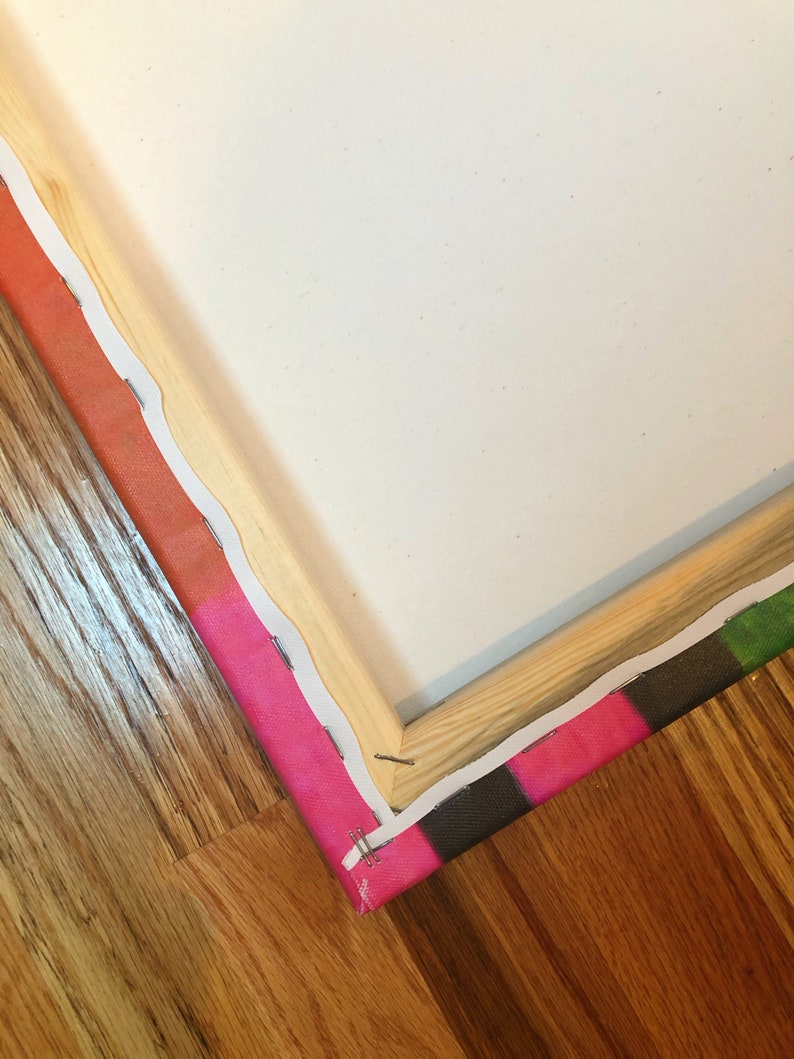 May include: Close-up of a corner of a canvas print with a wooden frame. The canvas is stretched tightly over the frame and secured with staples. The canvas is printed with a colorful abstract design.
