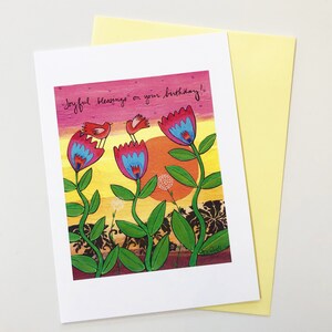 May include: A greeting card with a colorful illustration of three pink flowers with blue centers and two red birds. The card has the text "Joyful blessings on your birthday!" written in black cursive.