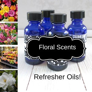 May include: Four small blue glass bottles with black lids and white labels. The bottles are filled with a clear liquid. The labels have a black and white design and the text "Floral Scents Refresher Oils!"
