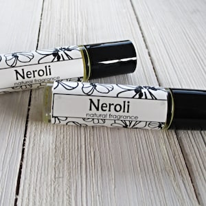 May include: Two small glass bottles with black roll-on tops. Both bottles have white labels with black floral designs and the text "Neroli natural fragrance".