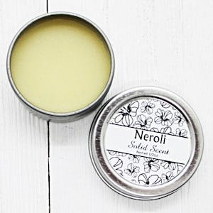 May include: A silver tin with a white label that reads "Neroli Solid Scent" and "Net wt 1/2 oz". The tin is open and a yellow solid scent is visible inside.