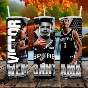 Puede incluir: Tres vasos térmicos negros y blancos con imágenes de jugadores de baloncesto. Los vasos tienen el texto "VICTOR WEMBANYAMA", "WEMBANYAMA" y "WEMBANYAMA" en ellos. Los jugadores de baloncesto llevan camisetas de los San Antonio Spurs.