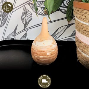 Peut inclure: Un vase décoratif en céramique avec une base arrondie et un long col fin. Le vase présente un motif marbré dans des tons beige et marron, créant une esthétique naturelle et terreuse. Un objet de décoration unique.