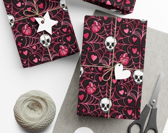 May include: Three gift boxes wrapped in pink and black wrapping paper with a skull and heart pattern. The paper features a spiderweb design.