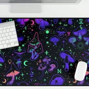 May include: A black desk mat with a repeating pattern of purple, pink, and green mushrooms and celestial symbols. A white keyboard and mouse are on the mat. The design includes stars and crescent moons.
