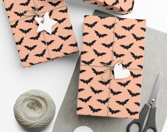 Op de afbeelding: Drie cadeaudozen verpakt in perzikkleurig papier met een zwart vleermuispatroon. De dozen zijn vastgebonden met touw en versierd met witte papieren sterren en harten.