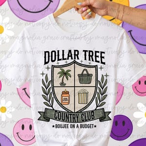 May include: A white short-sleeve t-shirt featuring a graphic of a shield divided into four sections containing a palm tree, a basket, a candle, and popcorn. The text reads Dollar Tree Country Club and Boujee on a Budget with laurel leaves.